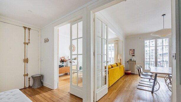 A spacious room with wooden flooring, a yellow sofa, and a dining area with metal chairs. - Parc Montsouris - Dans un joli square au calme - 2 chambres (Paris)