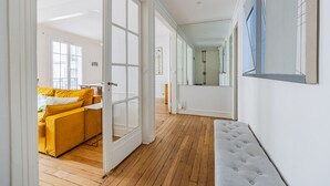 A spacious hallway with wooden flooring, a yellow sofa, and a grey tufted bench. - Parc Montsouris - Dans un joli square au calme - 2 chambres (Paris)