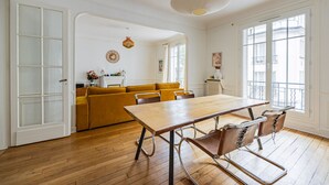 A spacious room with a wooden floor, a large table, and a yellow sofa. - Parc Montsouris - Dans un joli square au calme - 2 chambres (Paris)