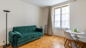 A room with a teal sofa, a dining table with chairs, a floor lamp, and a window with curtains. - Parc Monceau - Villiers - Studio (Paris)