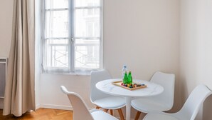 A room with a round white table, two white chairs, a window with a view of buildings, and a curtain. - Parc Monceau - Villiers - Studio (Paris)