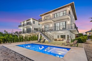 Una casa moderna de varios pisos con piscina, mobiliario exterior y una escalera que lleva a un balcón.
