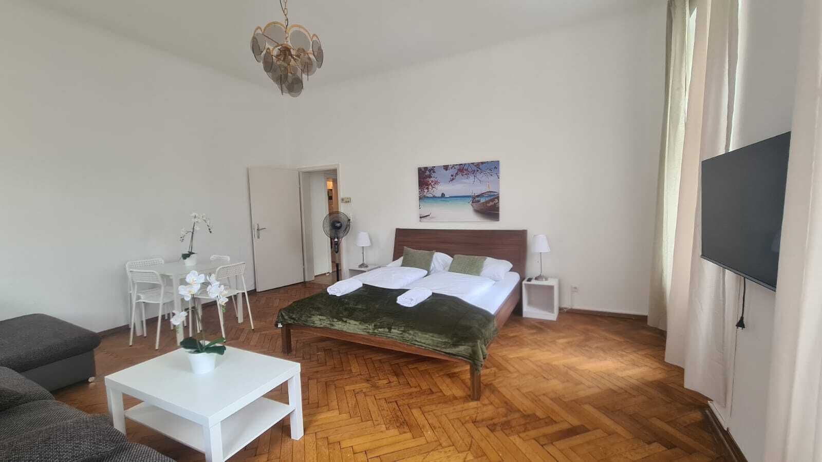 A hotel room with a bed, a desk, a chair, a fan, and a TV.