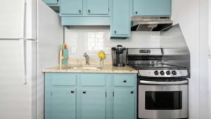 Une cuisine avec des meubles de couleur turquoise, un réfrigérateur blanc, une cuisinière en acier inoxydable et une machine à café.