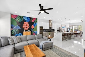 A modern living room with a grey sectional sofa, a wooden coffee table, and a vibrant tropical mural on the wall. - Modern 4BR Home with Rooftop Oasis (Sarasota)