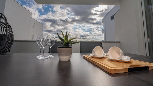 A dining area with a table set for two, a potted aloe vera plant, and a wooden cutting board with a knife. - Salt&Stone - apartment with private pool (Novalja)