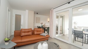 A modern living room with a brown leather sofa, a small round coffee table with vases, and a sliding glass door leading to a balcony. - Salt&Stone - apartment with private pool (Novalja)