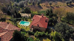 Vista aérea de uma propriedade com piscina, casa com telhado vermelho e áreas ajardinadas ao redor.