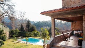 Um alpendre de pedra com piscina, rodeado por árvores e vista para colinas.