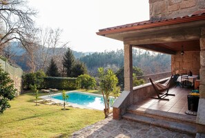 Eine Steinterrasse mit Pool, umgeben von Bäumen und Blick auf Hügel.