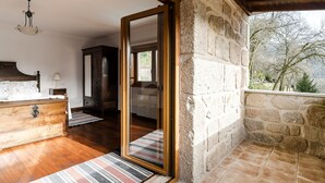 Um quarto com cômoda de madeira, espelho, abajur e parede de pedra.
