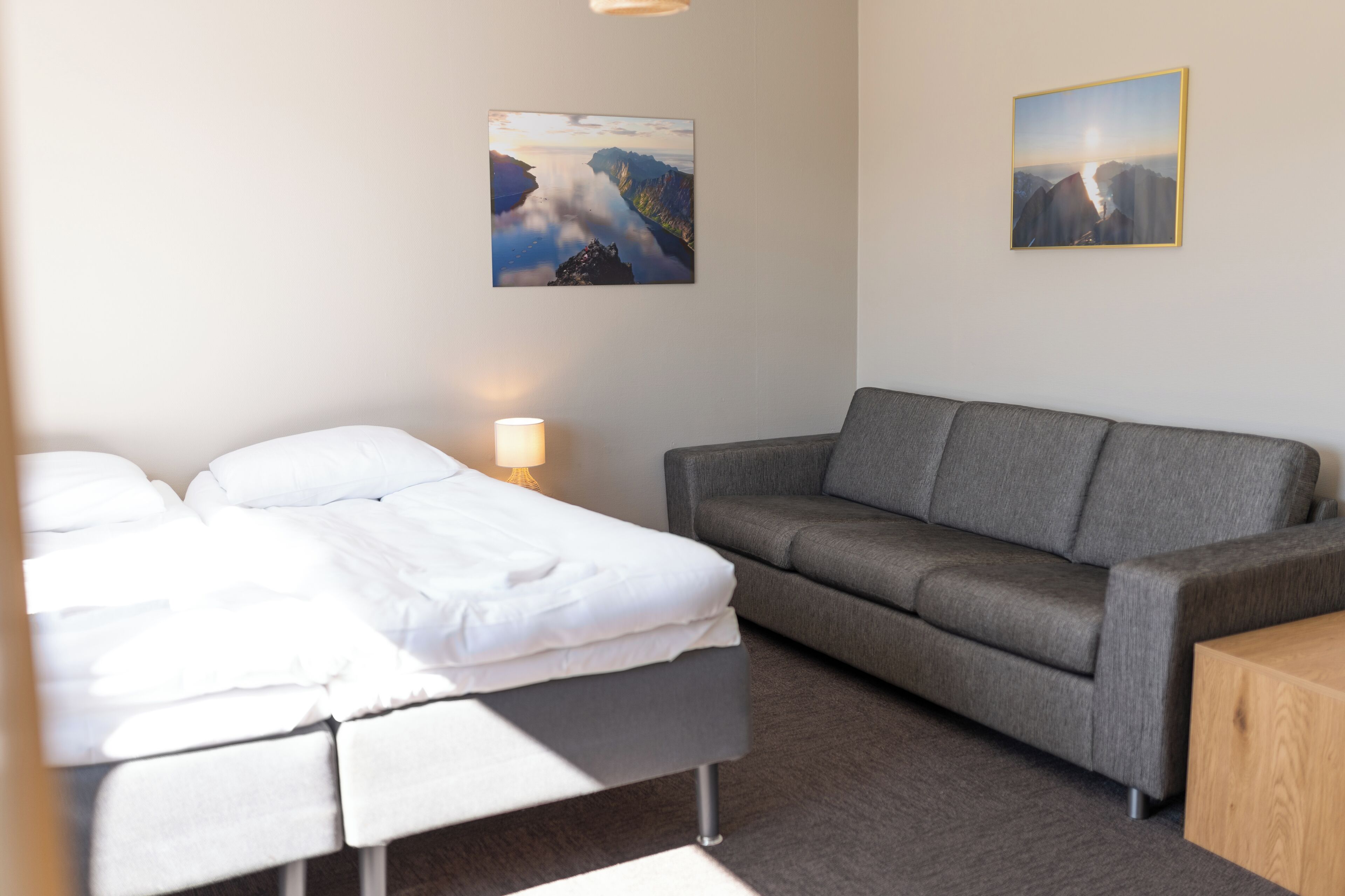Una habitación de hotel con una cama, un sofá gris, una mesita de madera y dos cuadros en la pared.