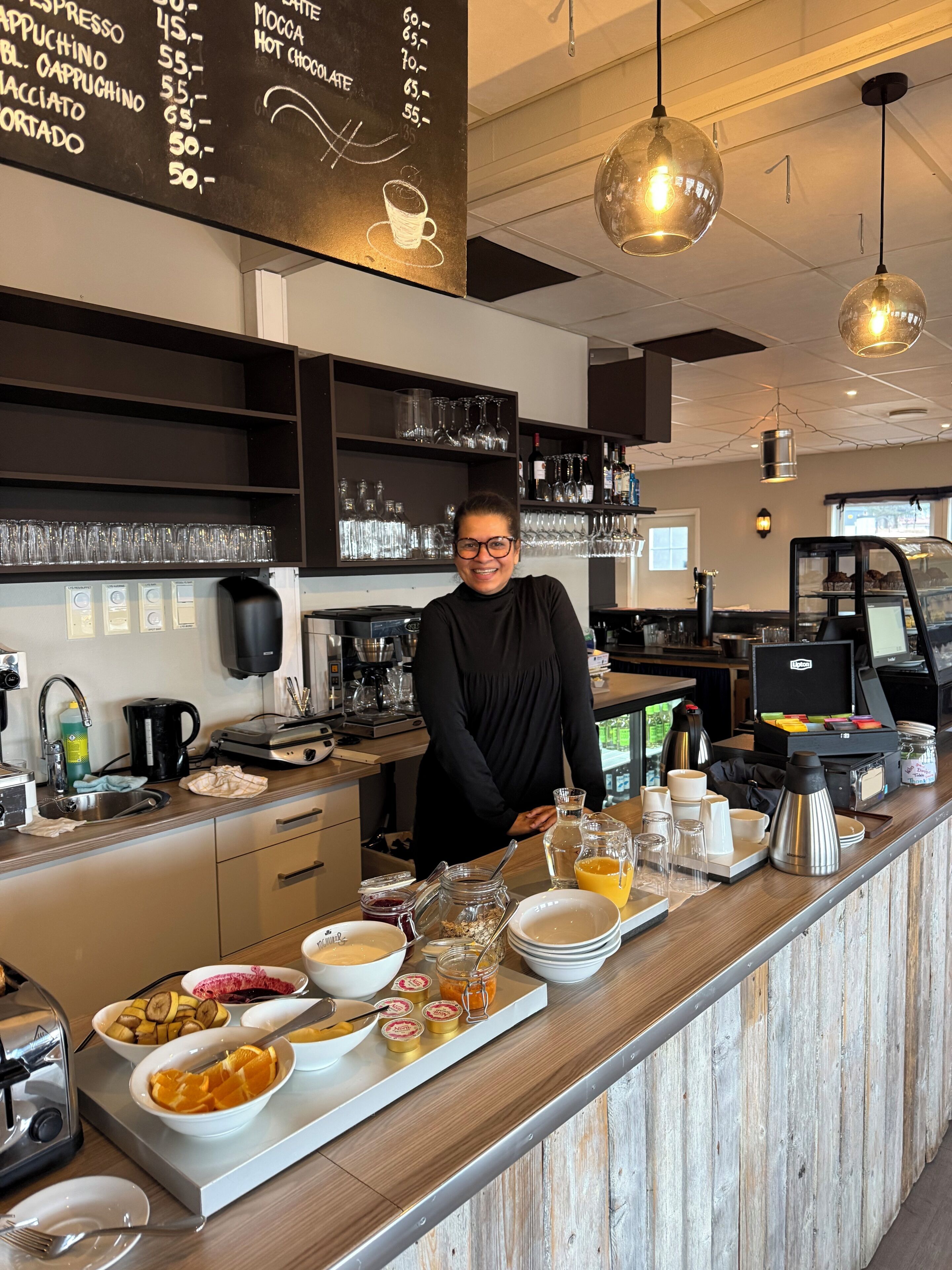 Um barista prepara café no balcão, com um menu, máquinas de café e vários copos e pires.