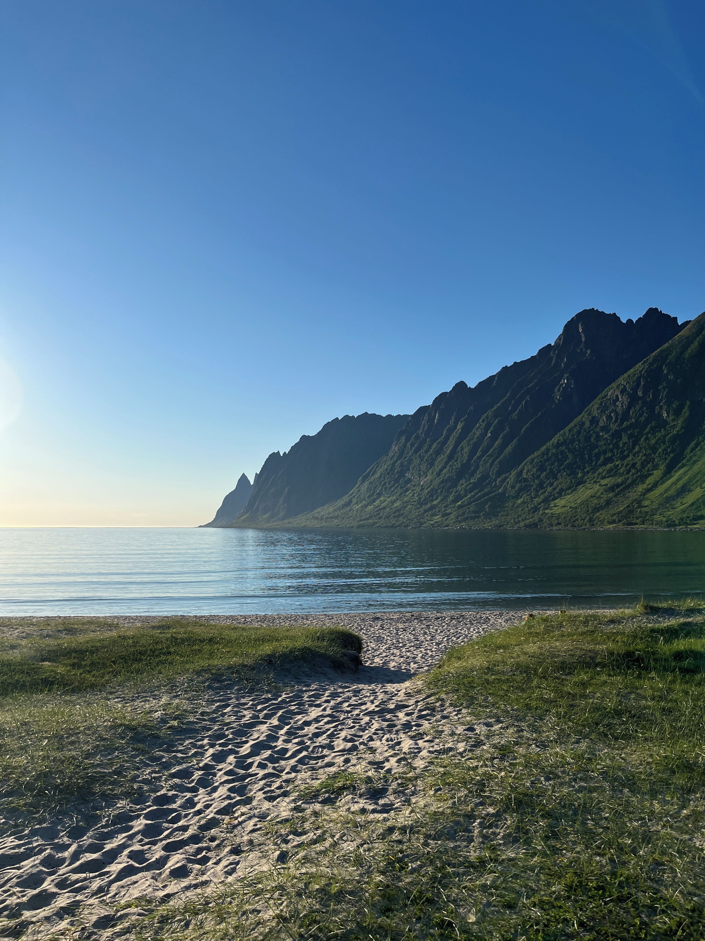 Una spiaggia con cielo sereno, un lago calmo e una montagna sullo sfondo.