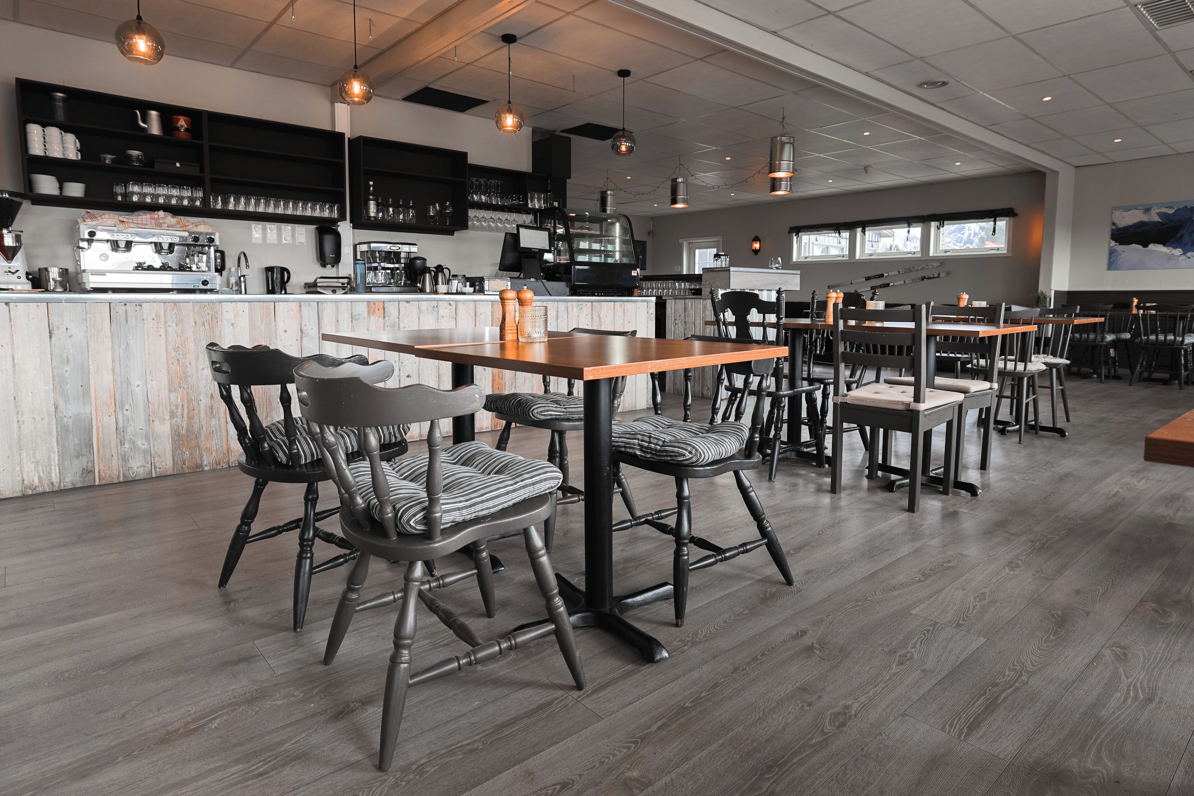 L'intérieur d'un restaurant moderne, avec un plancher en bois, des chaises à rayures noires et blanches, un bar doté d'étagères et une grande fenêtre.