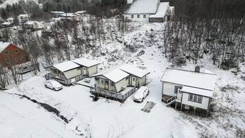 Un barrio residencial cubierto de nieve, con varias casas, un granero rojo y una ladera boscosa.