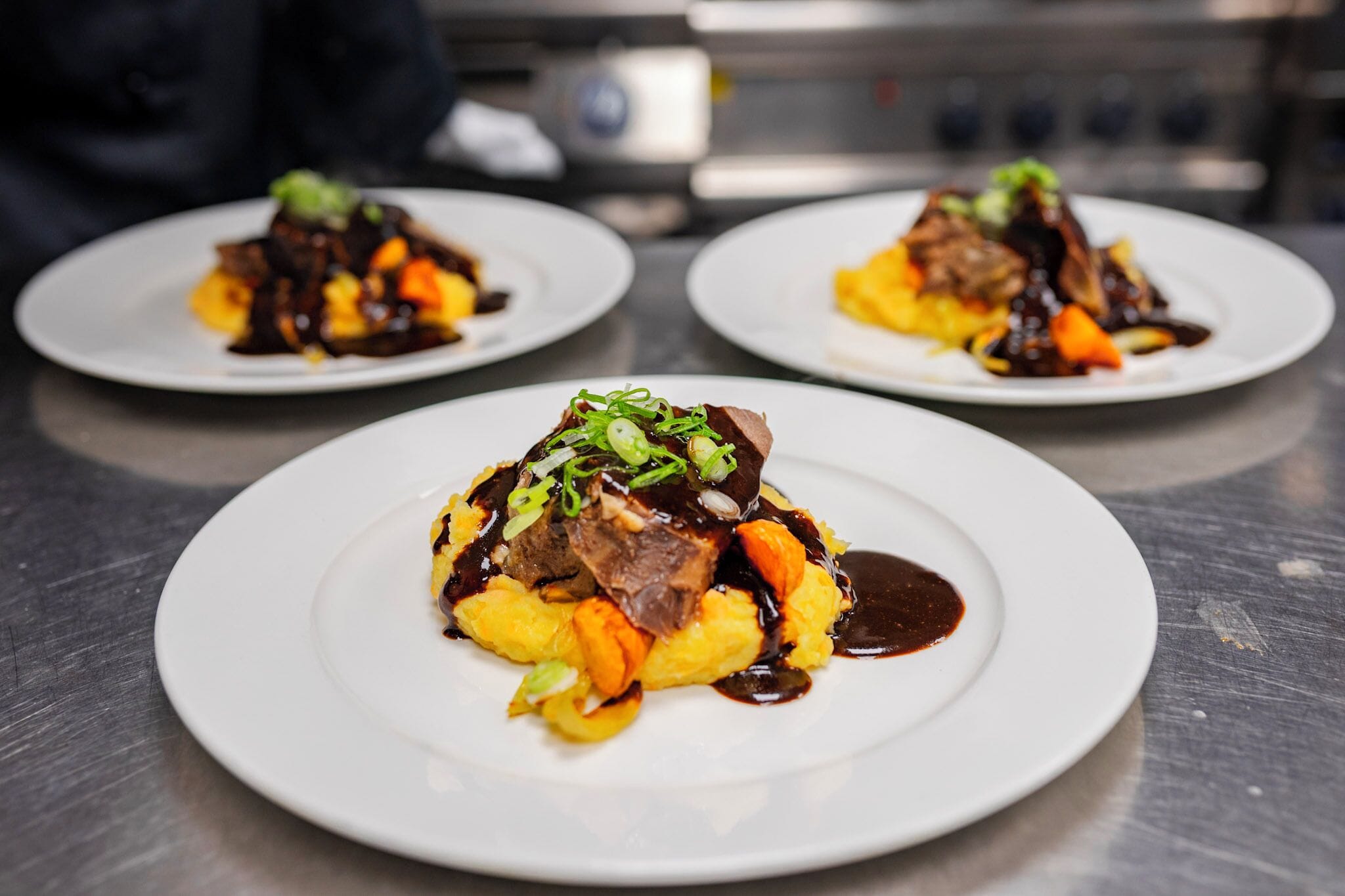 Three plates of food on a stainless steel table.