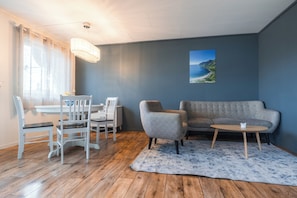 A living room with a sofa, chairs, a table, a rug, and a painting on the wall. - Yttersia Base (Senja)