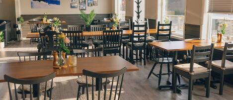 A restaurant with multiple tables and chairs, a large window, and a painting on the wall.
