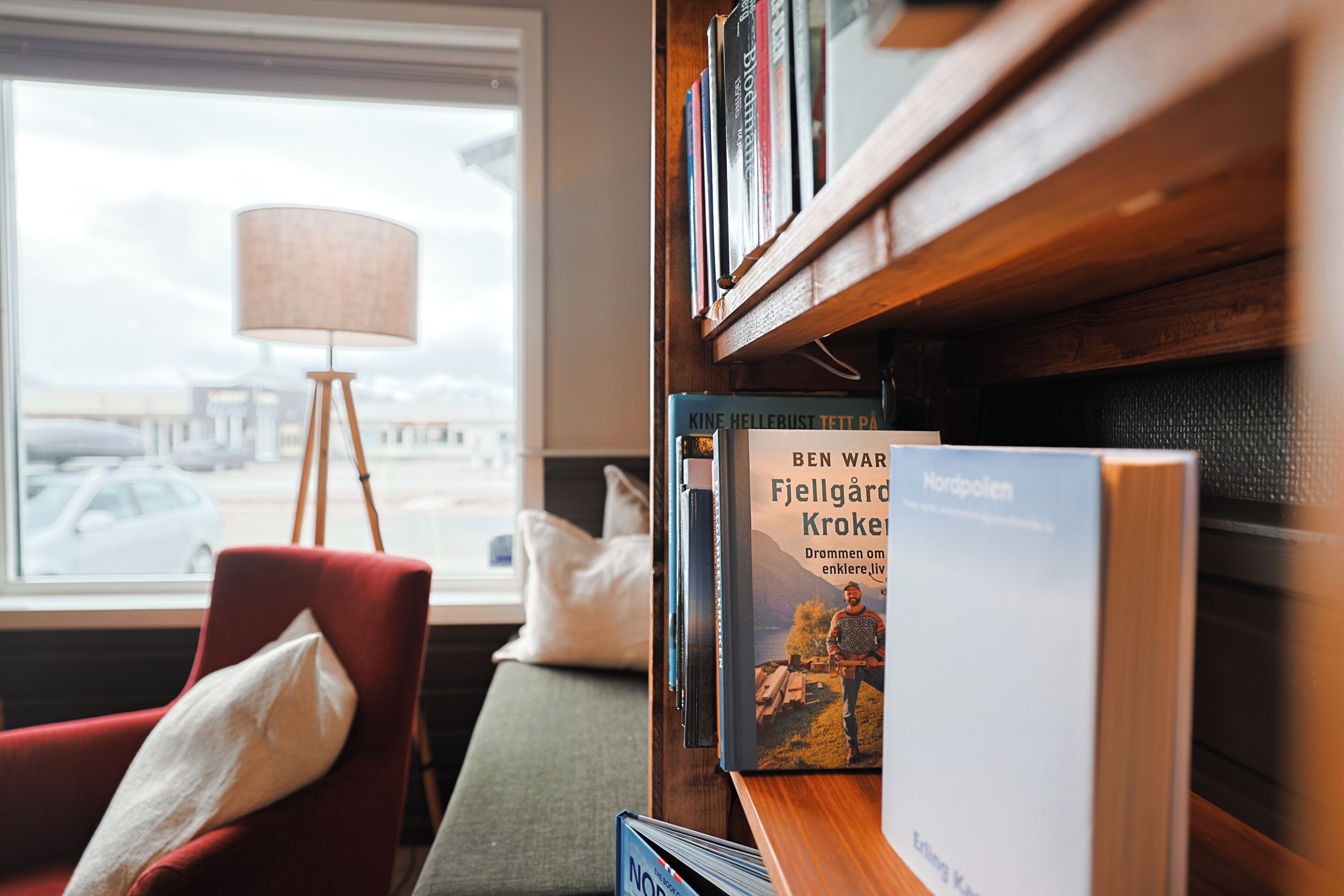 Una estantería con libros, una lámpara y un sillón rojo en una habitación con ventana.