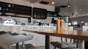 L’intérieur d’un restaurant avec une table en bois, des chaises à motifs rayés et des coussins, et un bar en arrière-plan.