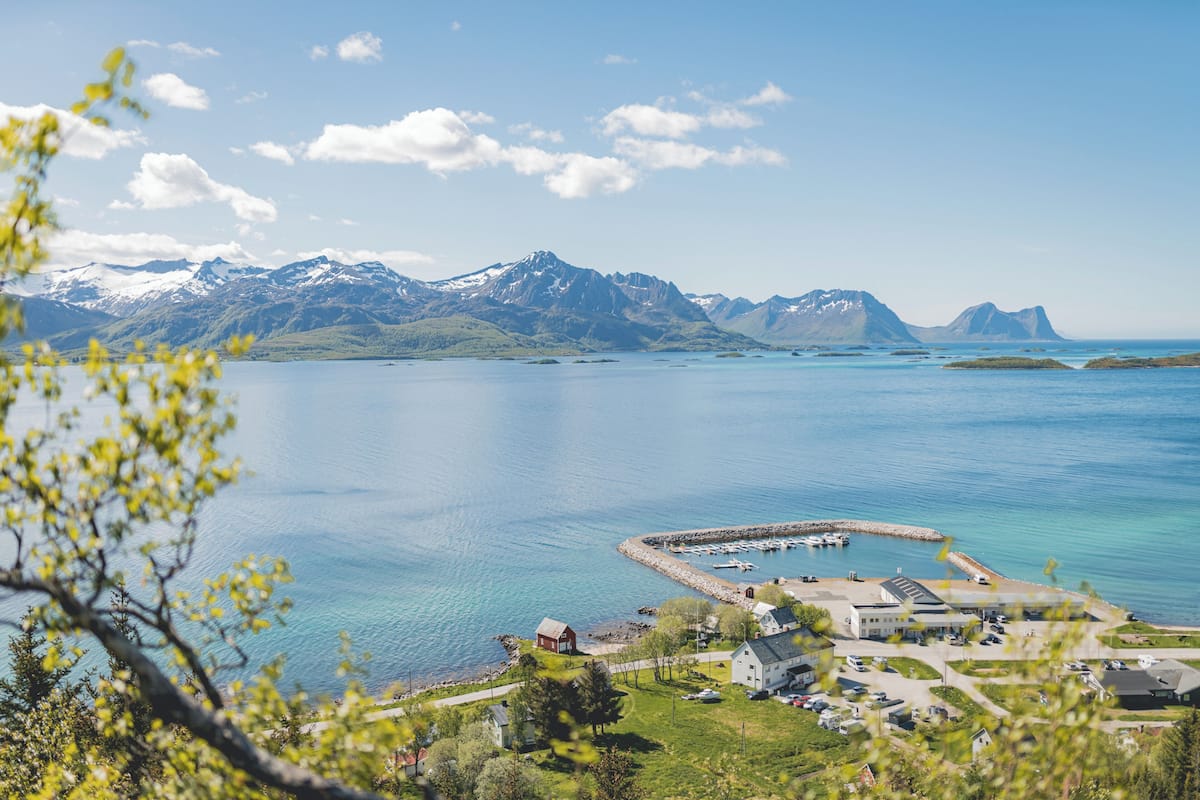 Landskab ved kysten med bjerge, en lysthavn og bygninger.