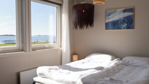 Une chambre à coucher avec un lit, une fenêtre donnant sur la mer et un tableau accroché au mur.