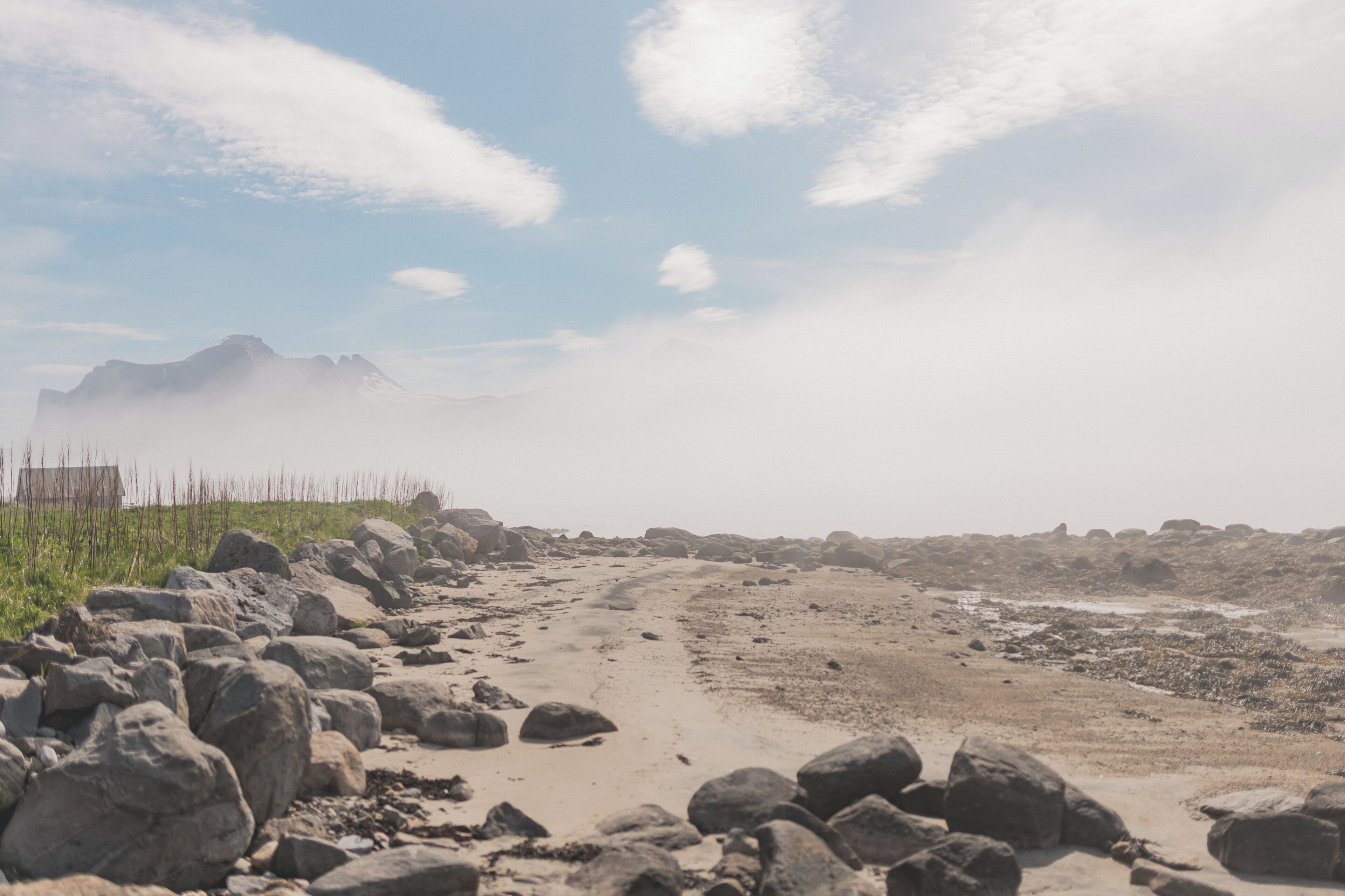 A rocky terrain with a dirt path leading towards distant mountains, a fence, and sparse vegetation.