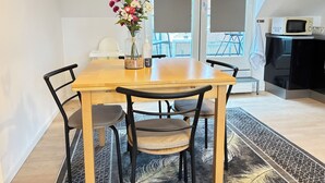 Un coin repas avec une table en bois, quatre chaises, un vase de fleurs et une vue sur l’extérieur grâce à de grandes fenêtres.