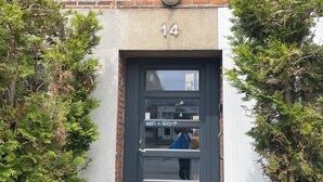 Un immeuble résidentiel à la façade en briques, avec une porte de couleur sombre portant le numéro 14 et une petite fenêtre située au-dessus de la porte.