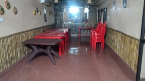 Un restaurante con sillas y mesas de plástico rojo, paneles de pared de bambú y un ventanal grande al fondo.