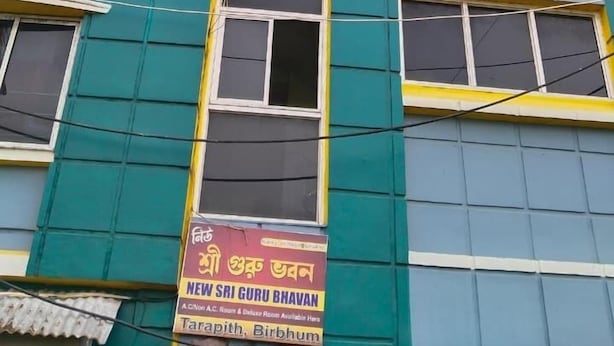 Un edificio de varios pisos con un letrero que anuncia "New Sri Guru Bhavan" y "Habitaciones con aire acondicionado/sin aire acondicionado y Habitaciones Deluxe".