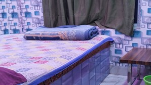 Un dormitorio con cama, cortinas, una ventana, una mesita y una cesta verde.