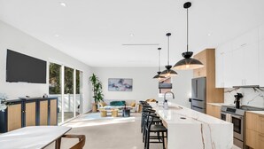 Une cuisine moderne dotée d’un îlot en marbre, de luminaires suspendus noirs et d’une grande fenêtre donnant sur une terrasse.