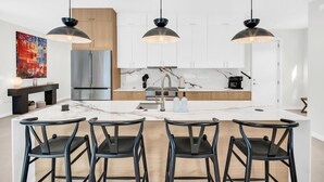 Une cuisine moderne dotée d’un îlot central, de luminaires suspendus noirs et d’un pare-feu en marbre.