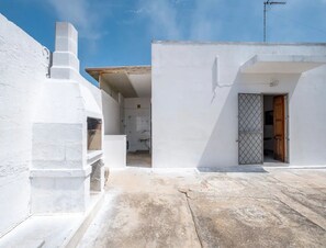 A white building with a small attached structure, a visible door, and a concrete ground.