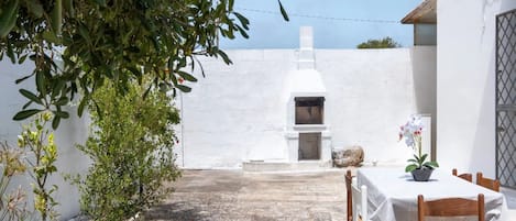 A white-walled building with a stone-paved patio, a table with chairs, and a potted plant.