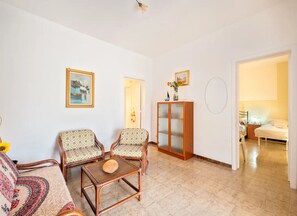 A living room with two patterned armchairs, a wooden cabinet, and a bed in the adjacent room. - Holiday Home 'Via Campania 3' with Private Terrace, Garden and Air Conditioning (Torre Lapillo)
