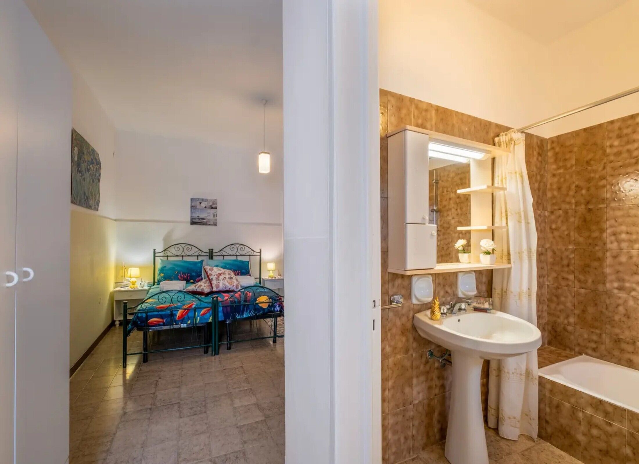 Een slaapkamer met een bed, nachtkastjes en een badkamer met een wastafel, spiegel en douche.