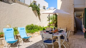 Een terras buiten met een eettafel, twee blauwe loungestoelen en een witte parasol.