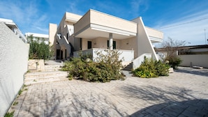 Een modern huis met twee verdiepingen, een plat dak, een balkon en een geplaveid binnenterrein.
