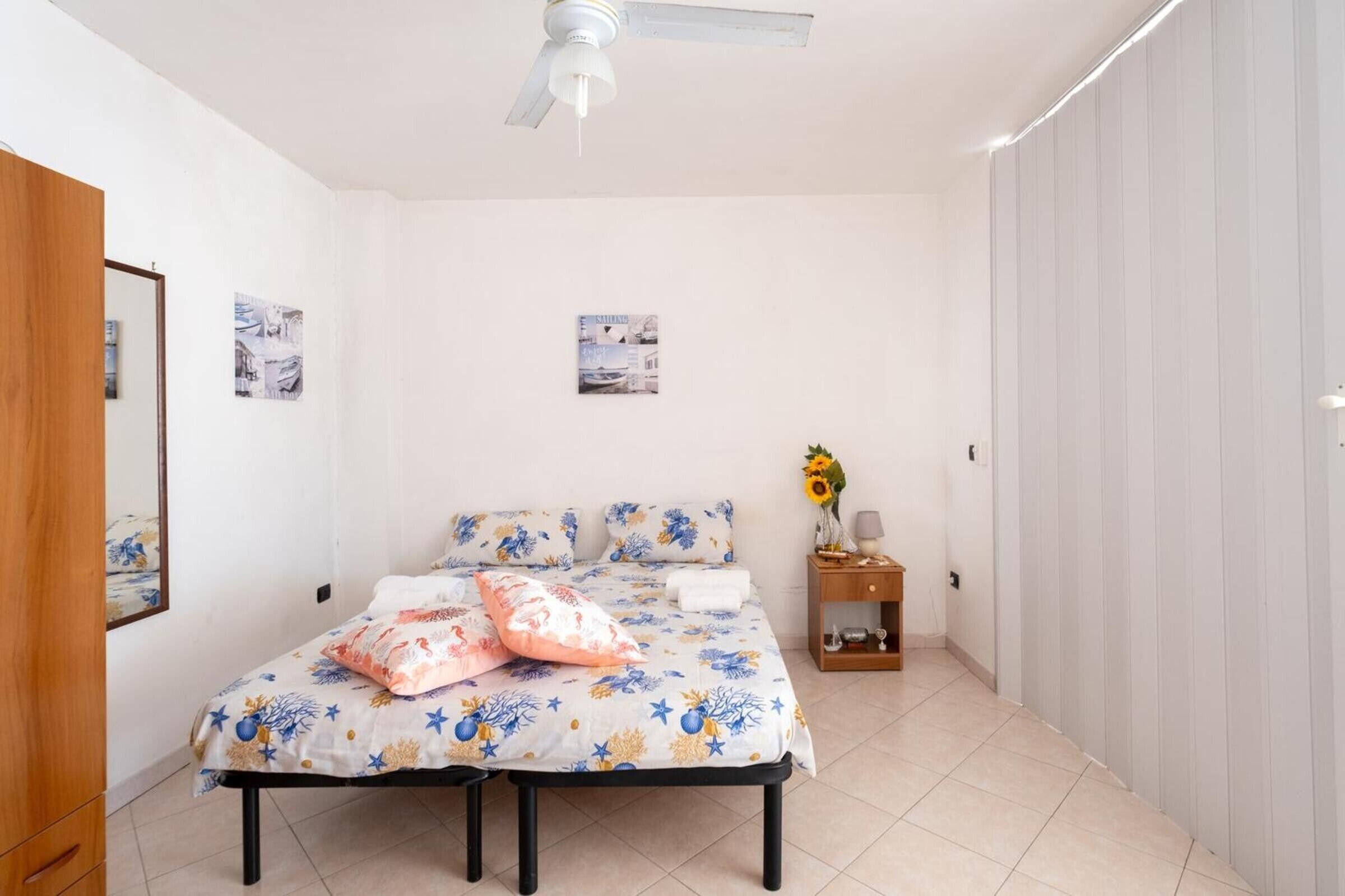 A bedroom with a bed, a nightstand, a ceiling fan, and wall-mounted pictures.