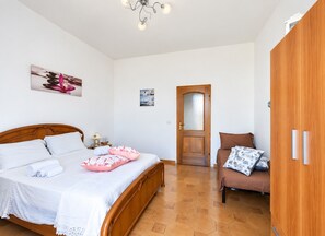Une chambre à coucher avec un lit en bois, une armoire en bois, un canapé marron et une porte dotée d’un panneau en verre dépoli.
