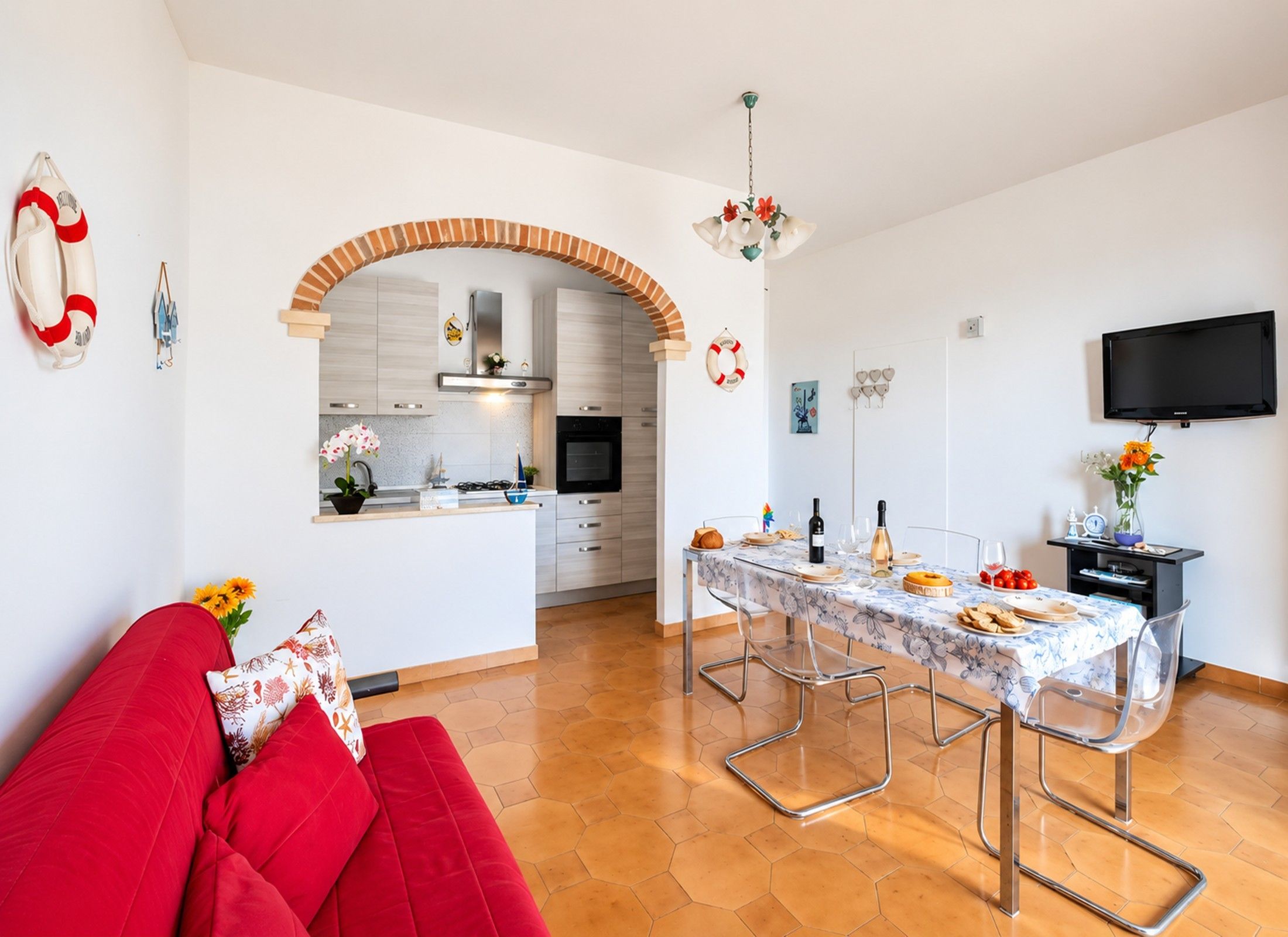 A modern kitchen with an archway, a dining area with a table set for two, and a red sofa.