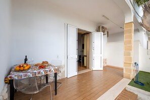 Huone, jossa on ruokapöytä katettuna, ovi, joka johtaa toiseen huoneeseen, ja pieni puutarha-alue.