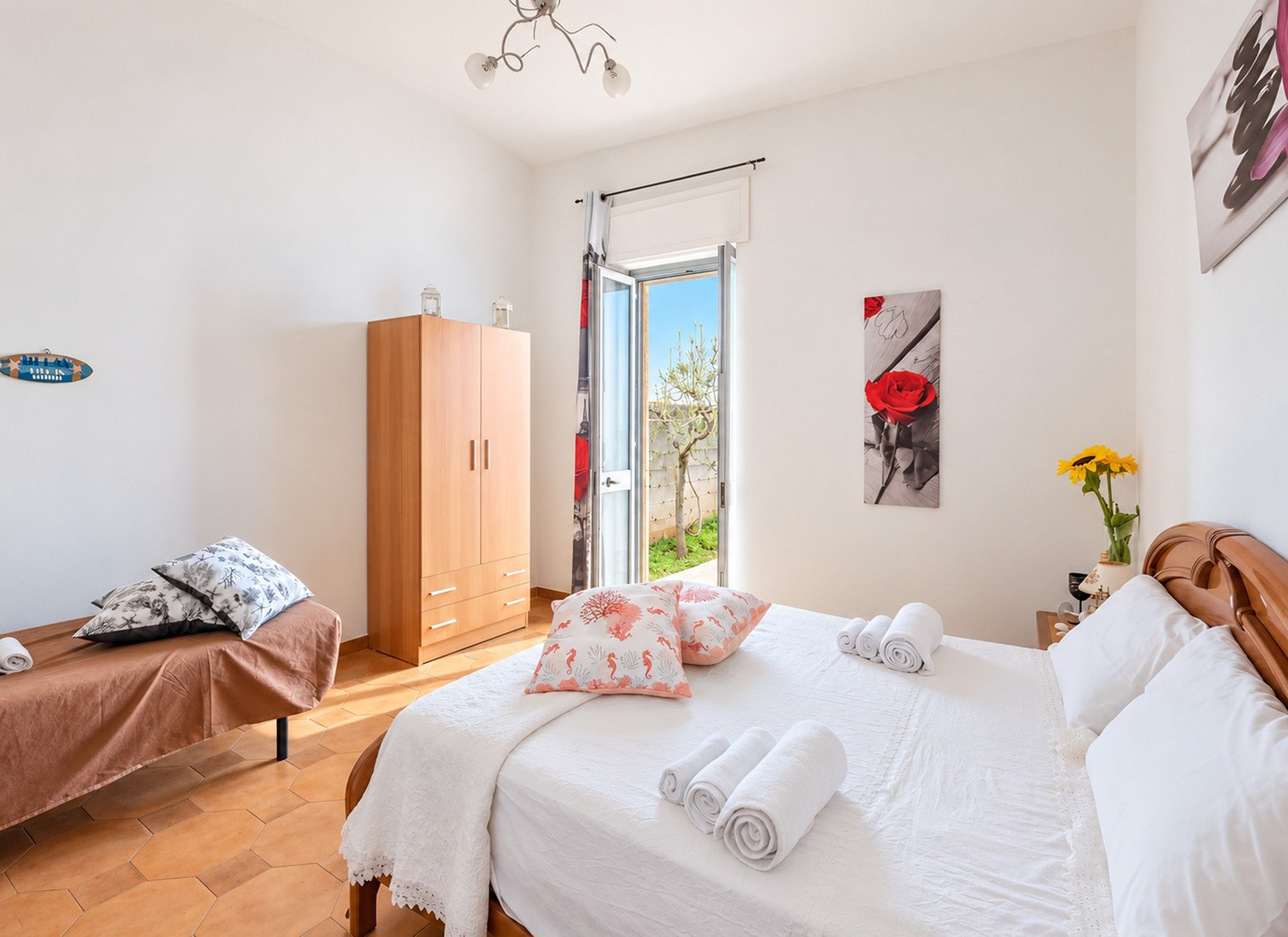 Ein Schlafzimmer mit einem Bett, zwei Nachttischen, einem Kleiderschrank und einem Fenster mit Blick auf Grünflächen.