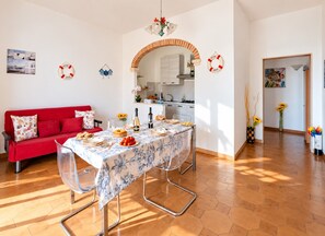 Un coin repas avec un canapé rouge, une table dressée pour quatre personnes et une cuisine en arrière-plan.