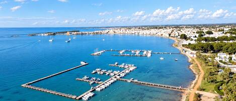 Un puerto costero con barcos amarrados, cielo azul despejado y una zona residencial al fondo.