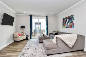 Een moderne woonkamer met een grijze bank, een witte fauteuil en een kleurrijk kunstwerk aan de wand.