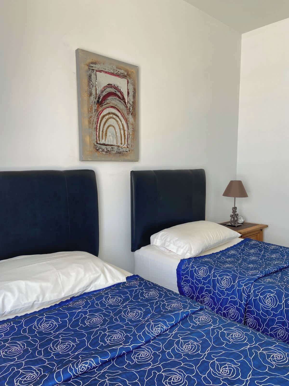 A hotel room with two beds, each with a headboard, a nightstand with a lamp, and a wall-mounted artwork.